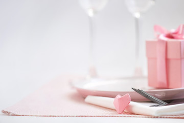 Dinner on Valentine's day. Pink plate, Cutlery, pair of glasses, gift, heart on the table. Copy space