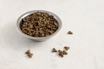 dry pet food for cats or dogs in a metal bowl on a light background with copy space