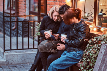 Three happy friends having a break with coffee sitting near a cafe outside.