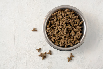 dry pet food for cats or dogs in a metal bowl on a light background with copy space, high angle view from above