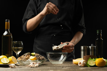 Chef salting oyster with lemon on the background of dry wine on a dark background, horizontal photo, menu, restaurant, Italian cuisine, Restaurant business