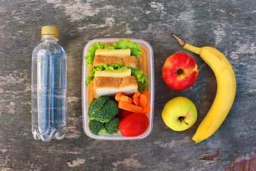 Foto op Aluminium Broodjes, fruit en groenten in voedseldoos, water op oude houten ondergrond. Bovenaanzicht. Plat leggen. © Viktoriia M