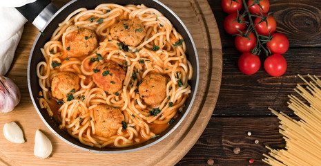 spaghetti with meatballs in a pan on a wooden background