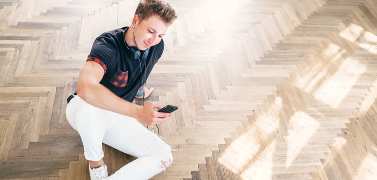 Young man using his smartphone with headphones, listen the music and sit on the floor