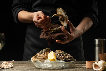 The chef opens and cleans the raw oyster against a background of white wine, lettuce, lemons and...