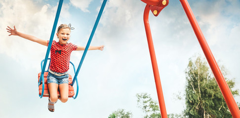 Happy little child girl laughing and swinging on a swing in the city park in summer - obrazy, fototapety, plakaty