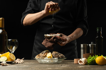 Chef watering raw oyster with lemon juice, with dry Italian wine, for cooking and cooking on a black background, Concept menu, cooking recipes, restaurant business, hotel business