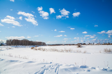 Winter landscape. Countryside. Frozen river. Sunny day. Blue sky. White clouds.