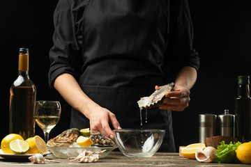 The chef opens and cleans the raw oyster against a background of white wine, lettuce, lemons and limes.