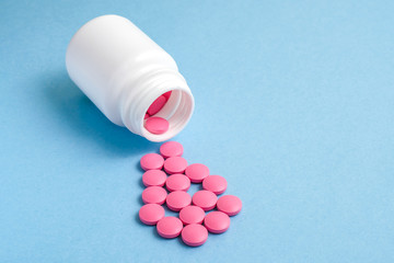 Pink pills fall out of a white container on a blue background.