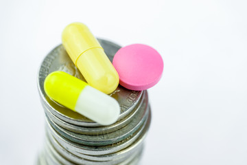 Yellow capsules and a pink pill on a stack of coins on a white background. The concept of business on drugs.