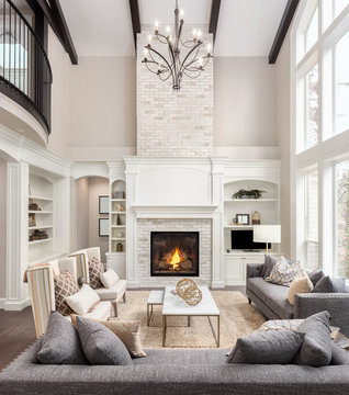 Beautiful Living Room In New Luxury Home With Fireplace And Roaring Fire. Large Bank Of Windows Hints At Exterior View. Vertical Orientation