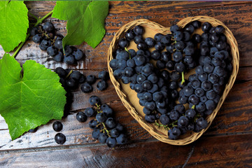bunches of grape inside basket with heart shape on wooden table