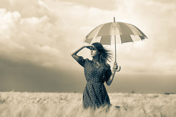 a young girl is standing on a wheat field with umbrella and waiting for rain. Image in old sepia...