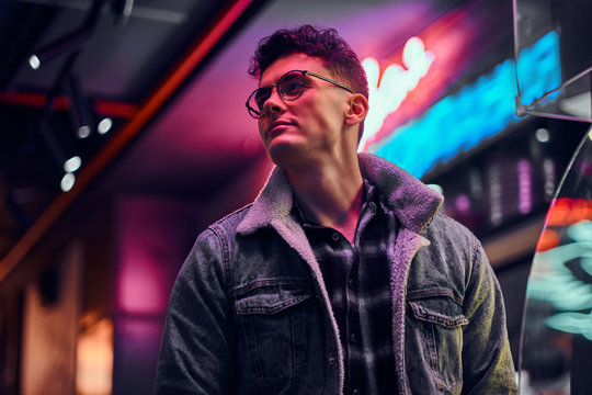 A Young Man Fashionably Dressed Standing In The Street At Night. Illuminated Signboards, Neon, Lights.