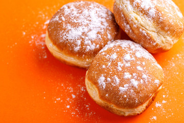 Tasty sweet donuts with powdered sugar on bright orange background