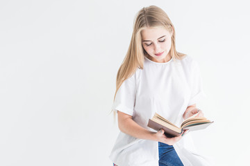 Portrait of a young stylish blonde girl in a white T-shirt and blue jeans reading a book on a white background