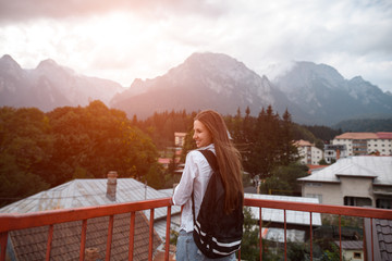 Fototapeta na wymiar Smiling hipster girl with backpack on background of mountains
