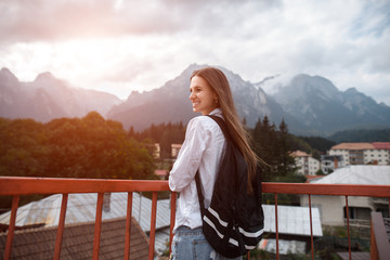 Smiling hipster girl with backpack on background of mountains
