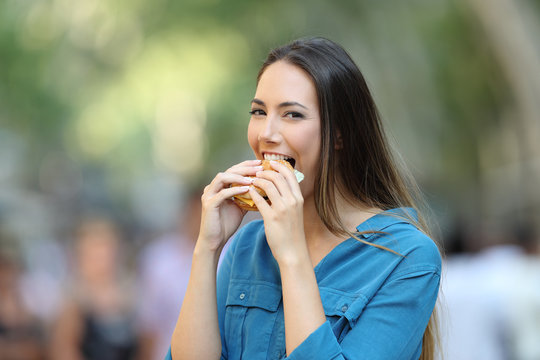 Happy woman biting a burger in the street