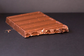 Bar of milk chocolate with crushed hazelnuts and alcohol raisins isolated on black background. Sweet confectionery delicasy.