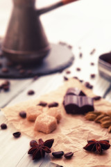 Close-up shot of coffee cezve with roasted beans, ground coffee, chocolate, badyan and cardamom on a wooden table.