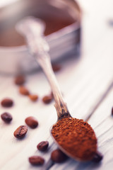 Macro shot of scoop of ground coffee in a silver spoon with roasted coffee beans on a wooden background.