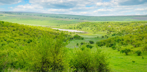 Fototapeta premium Green field and blue sky. Picturesque hills formed by an old river terrace. Moldova. Agricultural landscape. Wide photo.