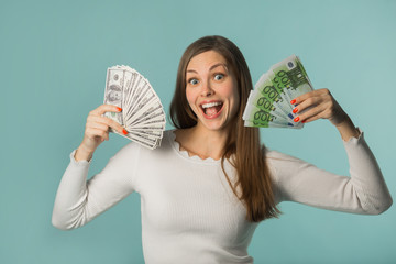 beautiful young girl holding bills with dollars and euros on a blue background