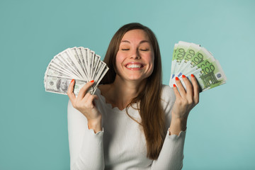 beautiful young girl holding bills with dollars and euros on a blue background