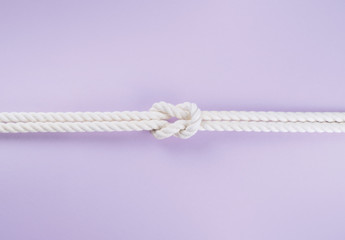 White ship ropes connected by reef knot on purple