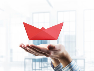 Origami boat in male palms against modern interior background. M