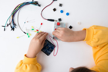 A cute girl constructs robot arduino and program it. The boards and microcontrollers are on the table. STEM education. Programming. Mathematics. The science. Technologie. DIY. 