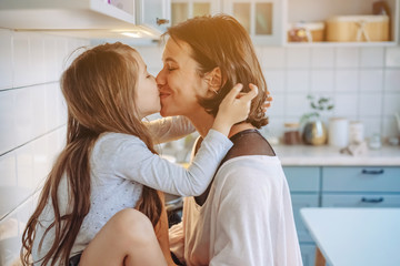 Mom kisses her little daughter in the kitchen