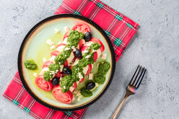 Tomato and mozzarella caprese salad and pesto sauce with olives on gray table