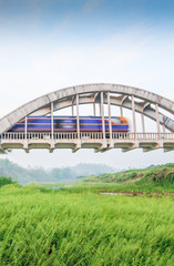 Train crossing Tha Chomphu ancient bridge in the morning.