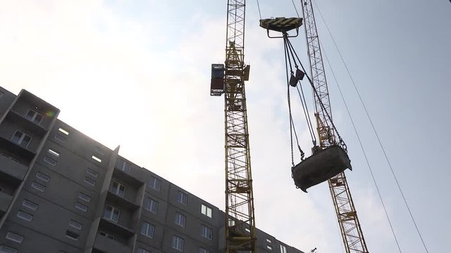 Construction site, crane lifting wall panel. Crane lifts heavy load on construction site. Crane lifting concrete mixer container against blue sky