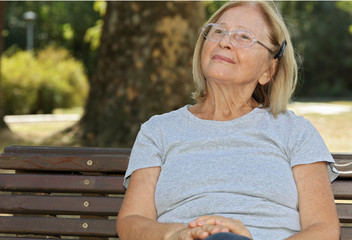 Pensive elderly woman daydreaming, relaxing in nature in park on sunny day. Outdoor portrait of...