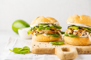 Grilled chicken and avocado burger on wooden board.