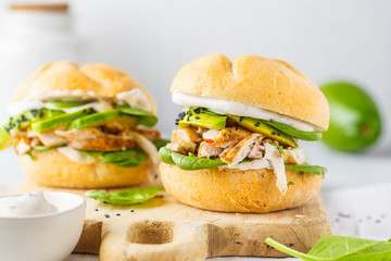 Grilled chicken and avocado burger on wooden board.