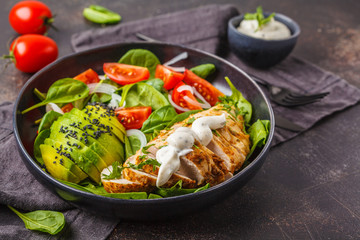 Chicken and avocado salad with spinach, tomatoes and Caesar dressing, dark background.