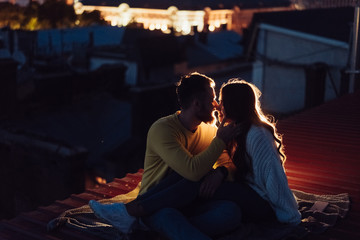 Loving couple is sitting on the roof of the house. Beautiful evening