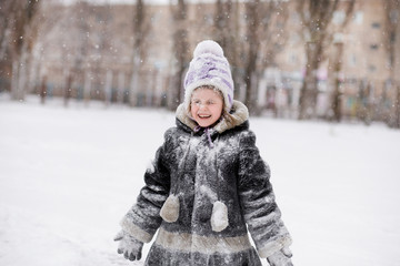 Fototapeta na wymiar Cute little girl covered with snow has fun in winter park,