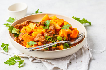 Spicy beef stewed with potatoes in tomato sauce in white plate. Meat traditional goulash.