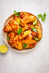 Spicy grilled chicken wings in tomato sauce in a white plate on a white background.