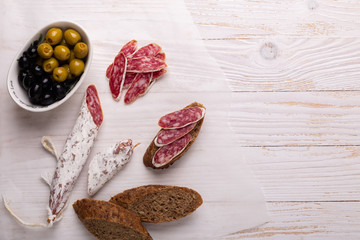 Salami and bread on white wooden background. Top view.