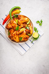 Spicy grilled chicken wings in tomato sauce in a white plate on a white background.