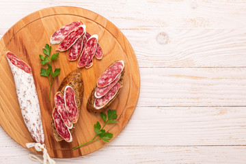 Salami and bread on white wooden background. Top view.