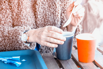 Hands brew a tea bag holding a disposable paper cup and a plastic spoon. Selective focus