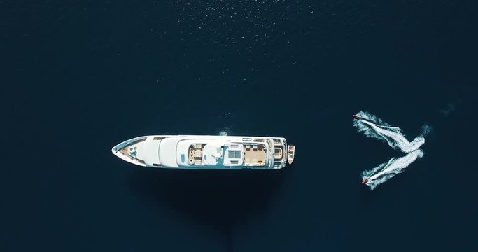 Top-down aerial view of a private luxury yacht in time as two jet-ski draw a heart round the boat
